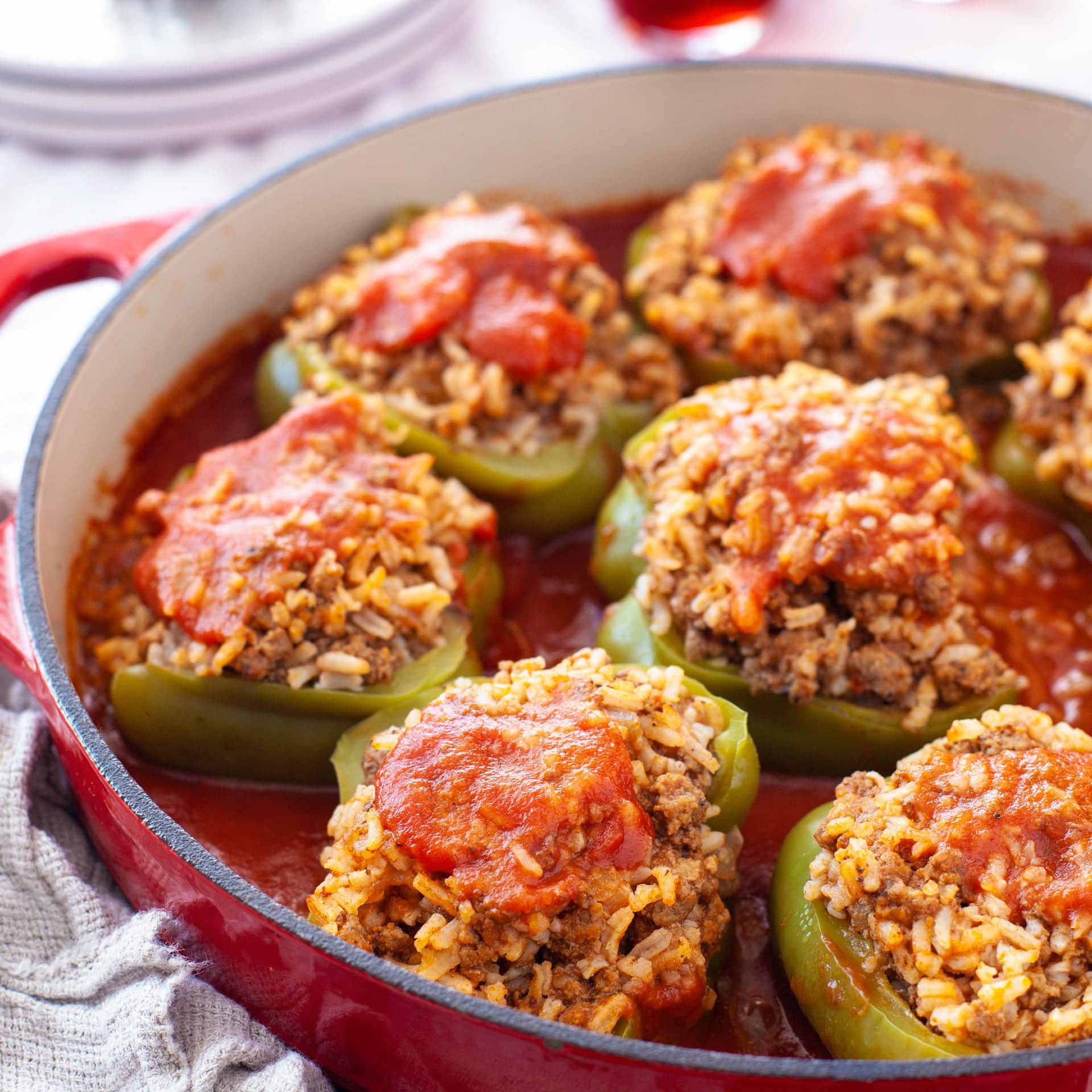 A shallow red Dutch oven filled with old fashioned stuffed bell peppers in a red sauce