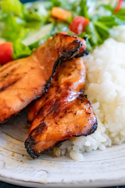Grilled Teriyaki Chicken thighs next to rice and salad on a white plate