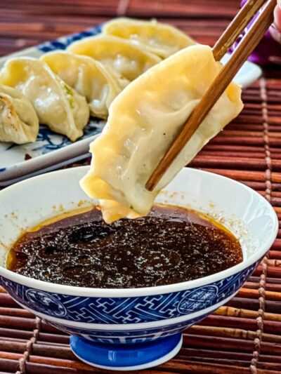 Chopsticks holding a cooked gyoza and dipping it into a blue bowl filled with potsticker sauce.