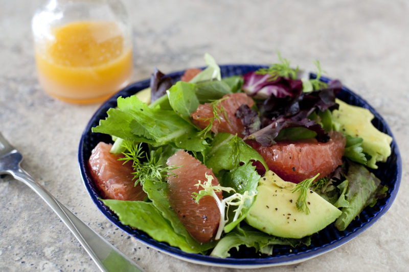 A fresh mixed greens salad with ruby red grapefruit and avocado on a dark blue plate.