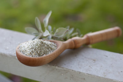 wooden spoon full of aromatic seasoning salts resting on a banister with fresh sage branches in the background