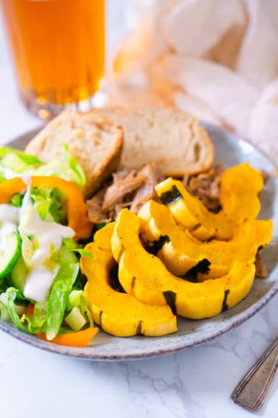 roasted delicata squash on blue plate with salad, bread slices, and pulled pork