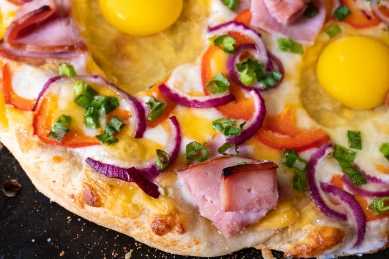 Breakfast pizza half cooked with raw eggs added on top