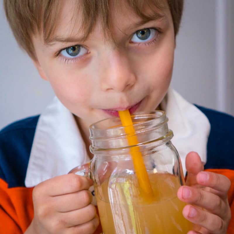 Boy drinking apple juice in glass jar with silicone straw
