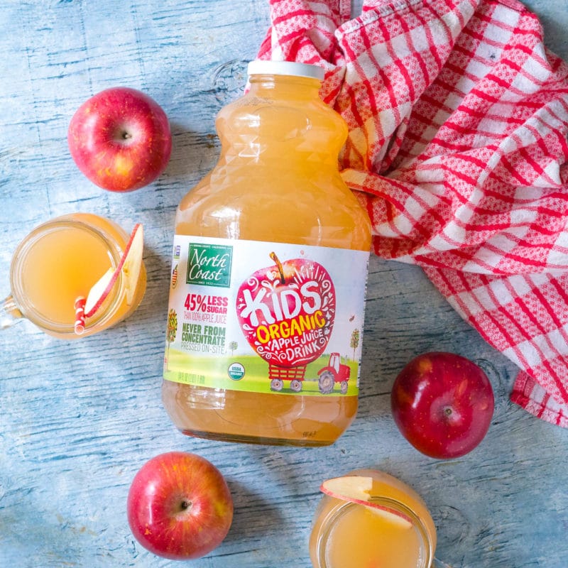 Jar of North Coast Organic Kid's Apple Juice Drink with glasses of apple juice and apples