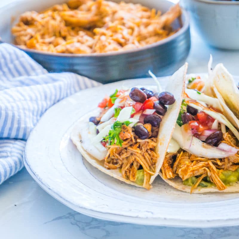 Crockpot Chicken tacos with slaw and black beans with shredded chicken in a bowl in the background