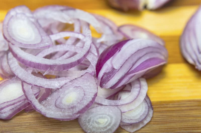 Close up of sliced red onion on wooden cutting board.