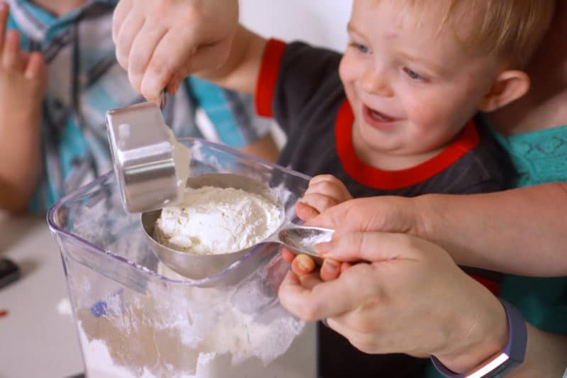 Toddler measuring flour with mom holding his hands