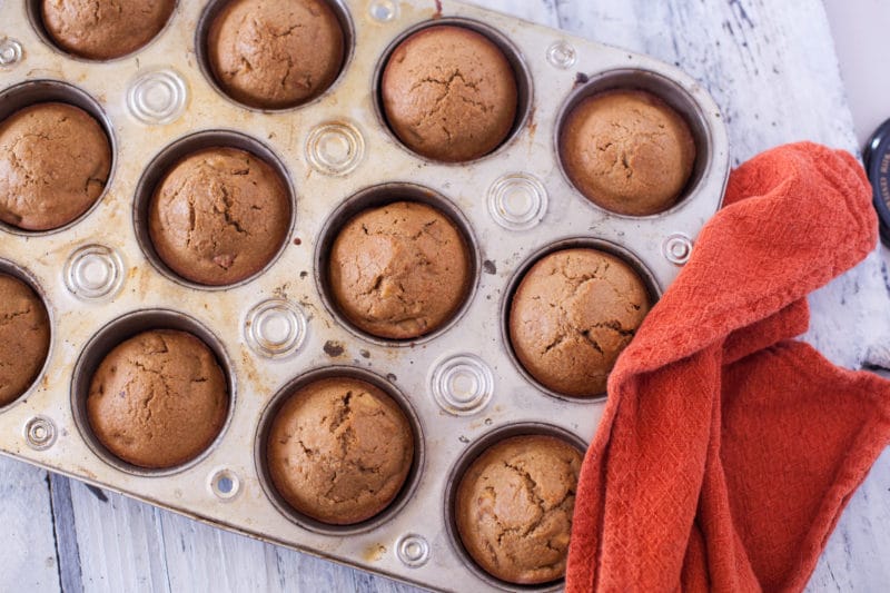 Overhead of Healthy Apple Muffins in a muffin tin with orangey red towel