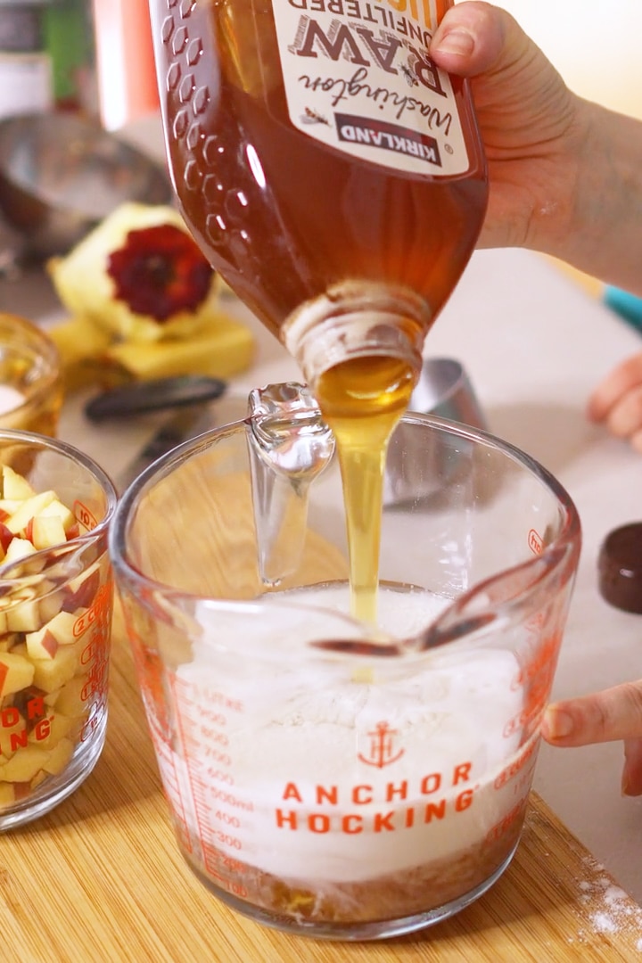 Pouring honey into glass measuring cup of wet ingredients for apple muffins