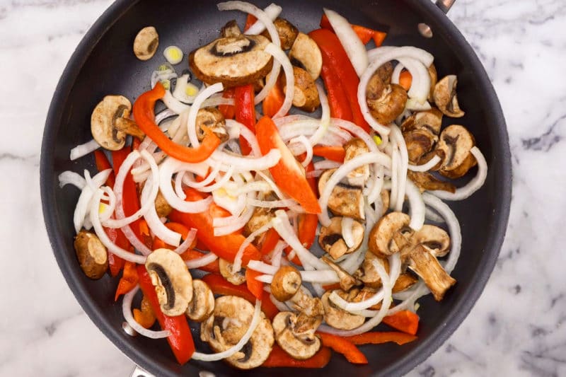 Sliced peppers, onions, and mushrooms in skillet