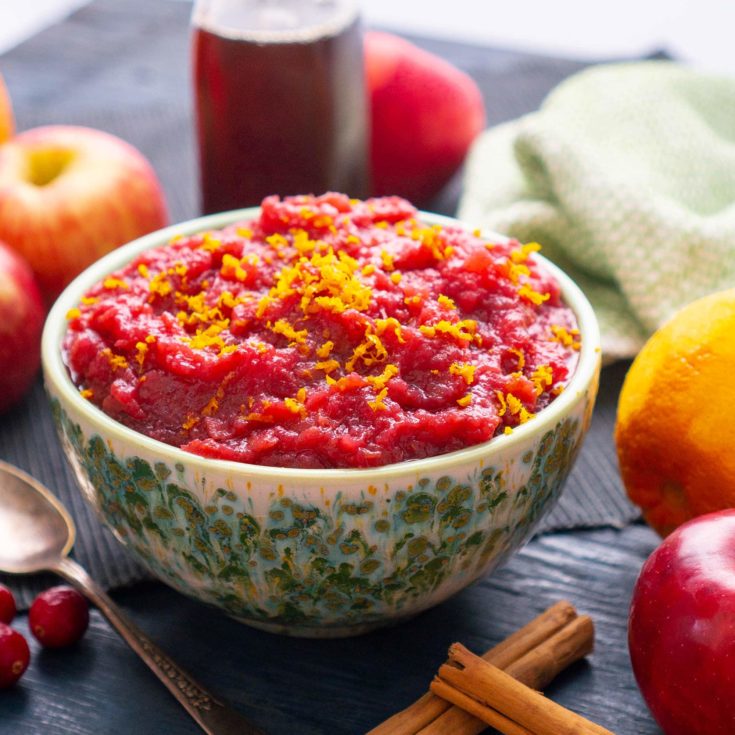 cranberry applesauce in a green bowl surrounded by ingredients