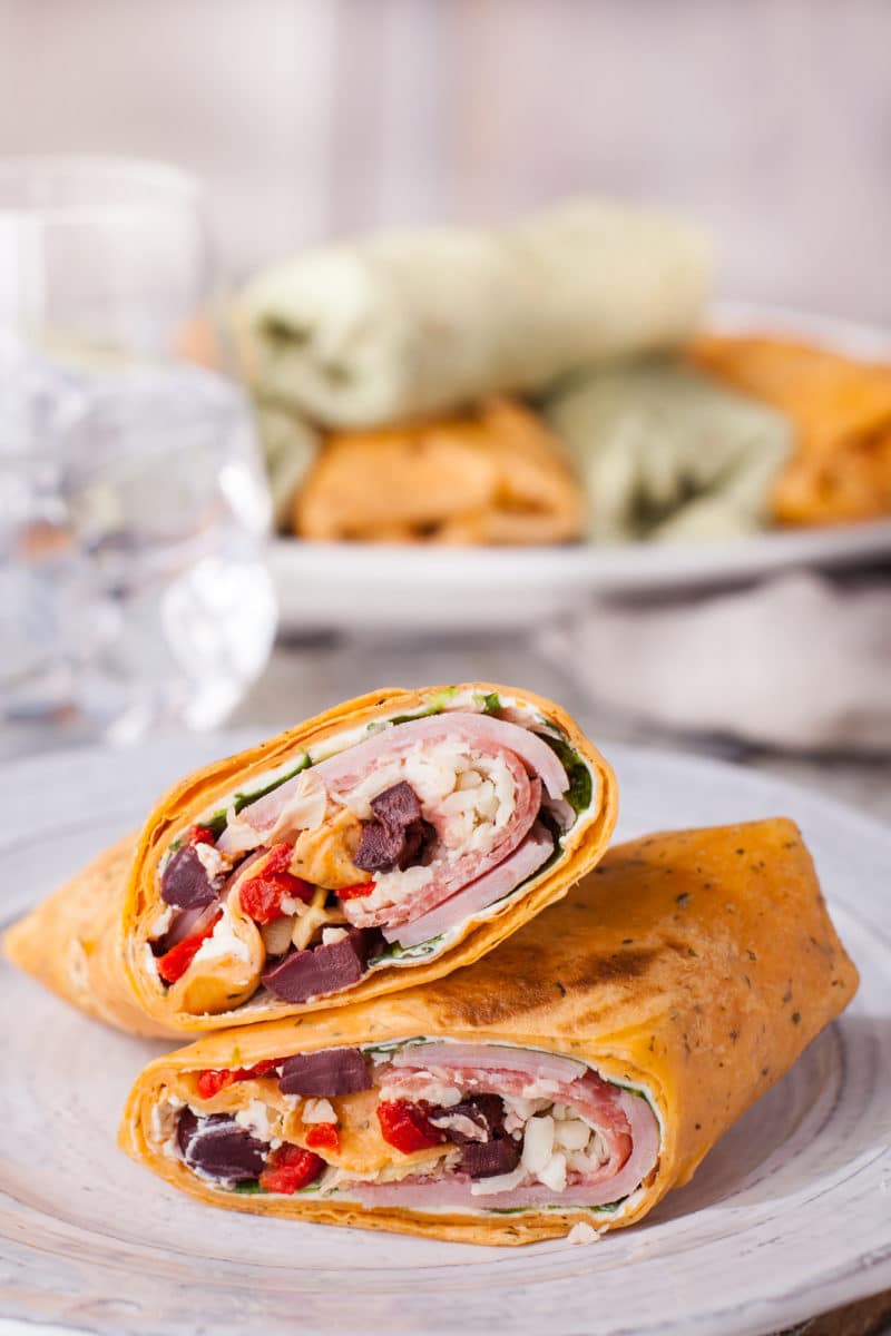 Two halves of Italian wrap stacked on each other on a white plate with whole wraps in the background