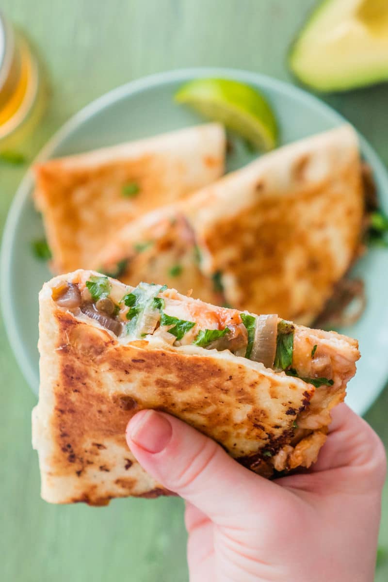 hand holding a slice of a BBQ chicken quesadilla above a plate of more slices