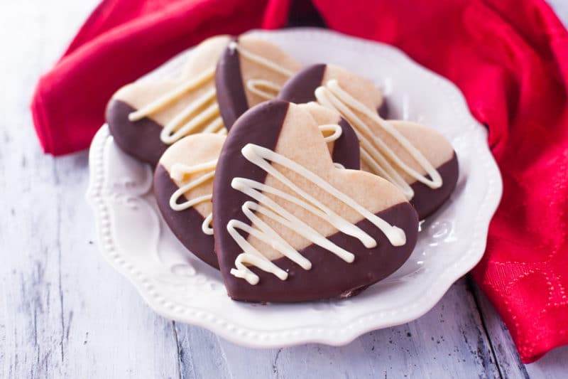 Fancy white plate full of Valentine's Day Sugar Cookies shaped like hearts, dipped in chocolate, and drizzled with white chocolate.