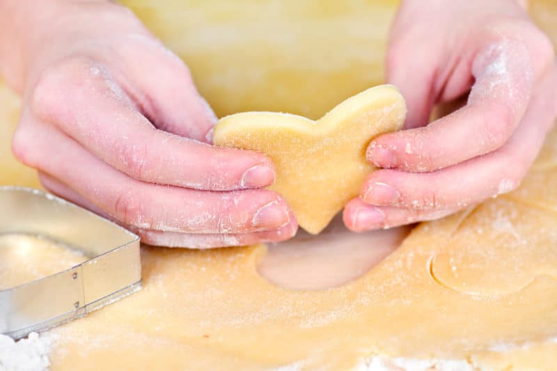 Hand holding cut out heart shape of  dough for Valentine's Day Sugar Cookies