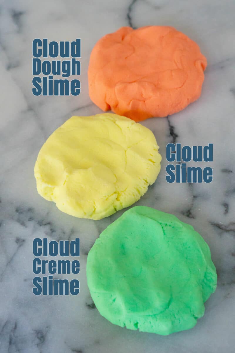 Three different discs of slime lay on a white and grey marble board. The textures look similar but the orange slime is labeled cloud dough slime, the yellow slime is labeled cloud slime, and the green slime is labeled cloud creme slime.