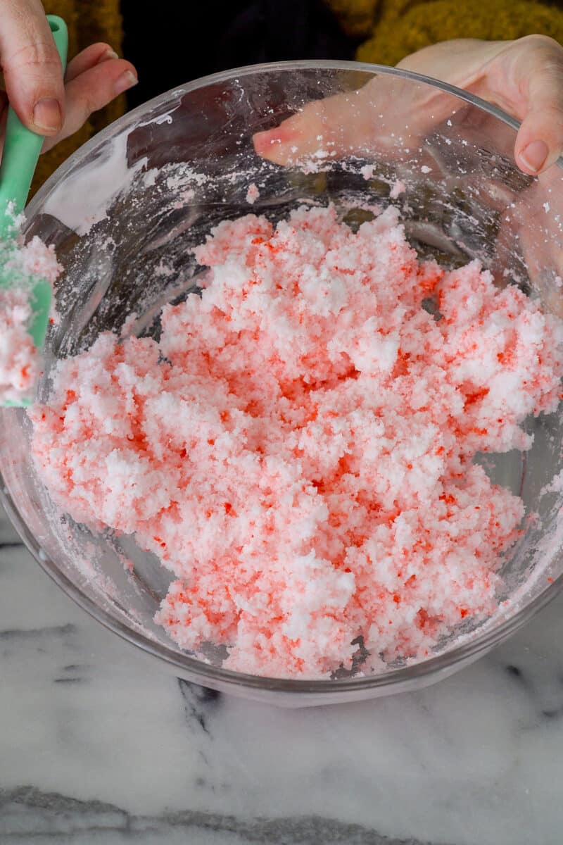 A woman's hands tip a large clear bowl to the camera to show the cloud slime ingredients she has mixed slightly so they resemble cottage cheese with red and pink speckles.